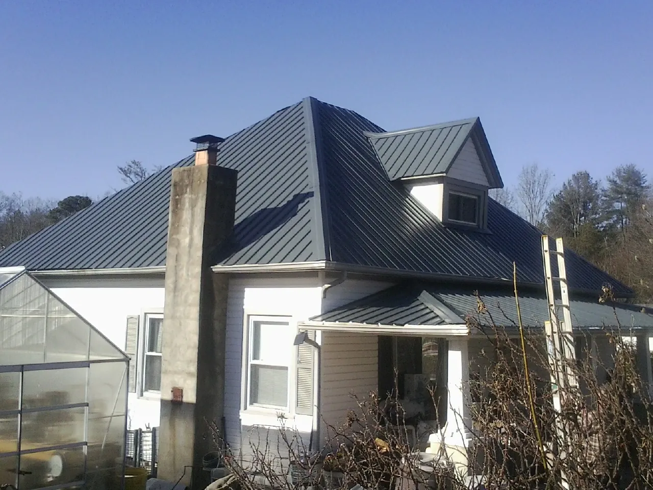 Dark blue standing seam metal roof on a white farmhouse with dormer — Slate & Tile Roof Repair by Roofing Brothers in Harbeson