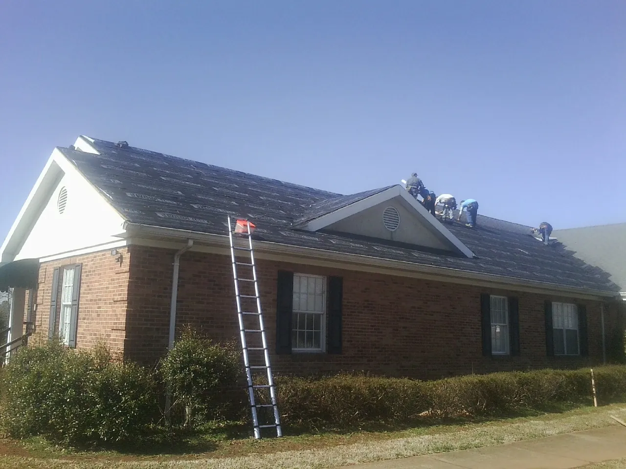Crew tearing shingles off a brick ranch roof with a ladder set — Metal Roof Repair work by our crew in Harbeson