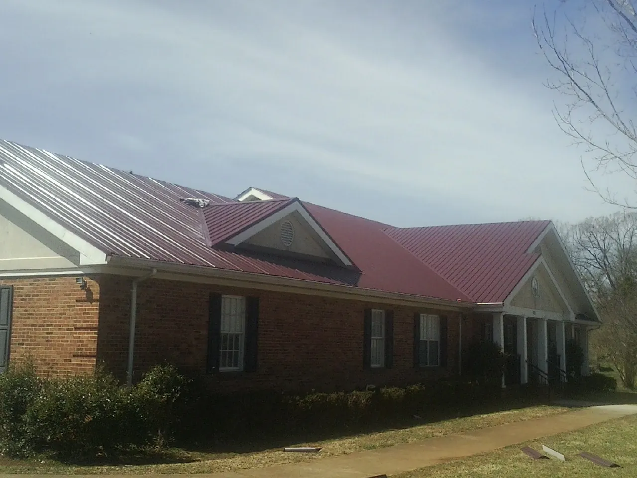 Red metal roof with gabled entries on a long brick building, from a Hail Damage Roof Repair job in Harbeson