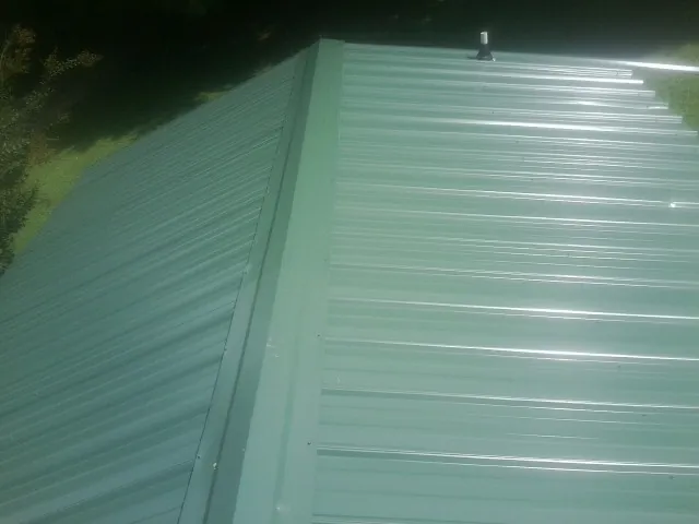 New green metal panels meeting at the ridge of a roof — Flat Roof Repair work by our crew in Harbeson