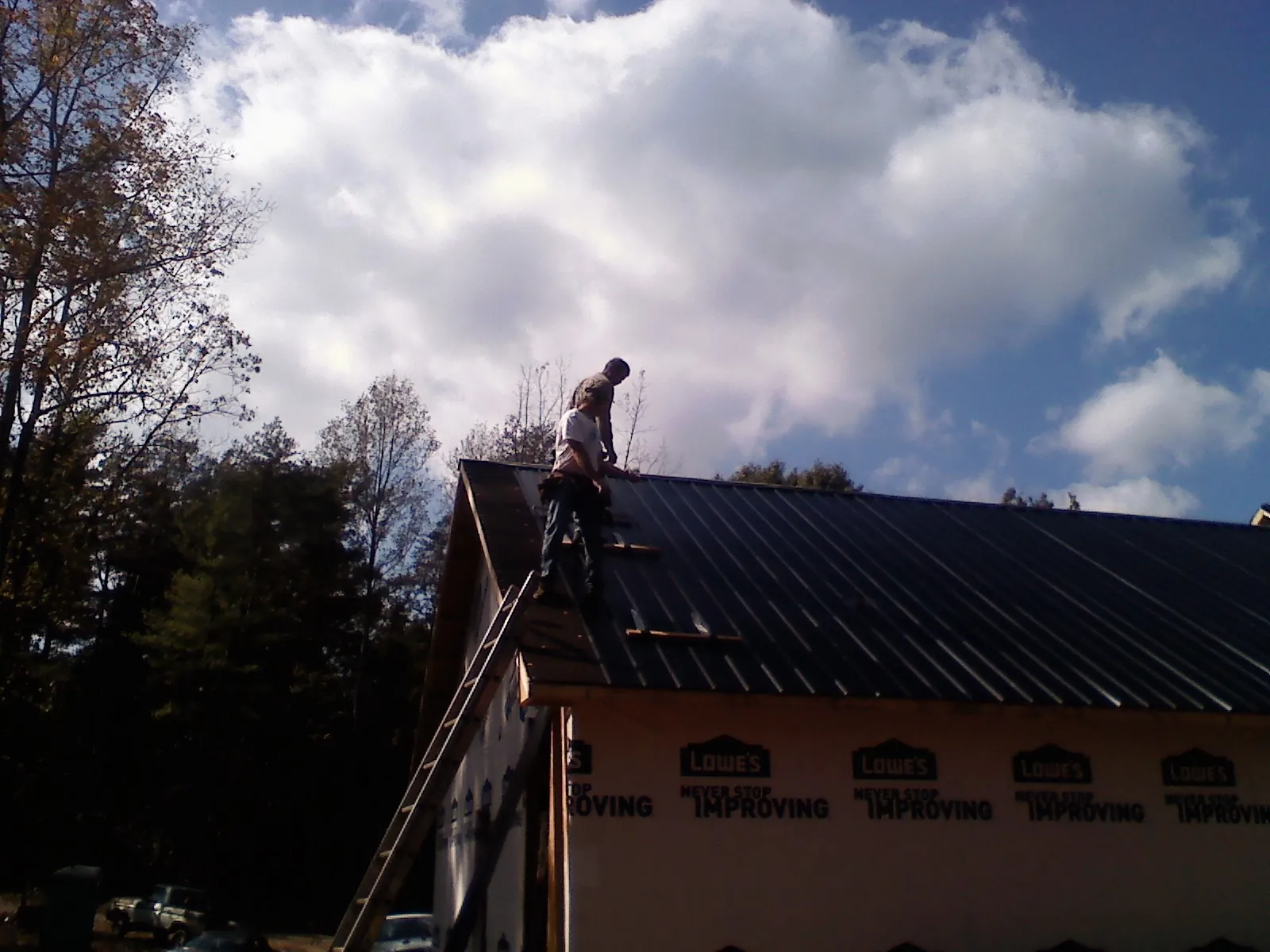 Roofer fastening dark metal panels high against a cloudy sky, from a Roof Inspection job in Harbeson