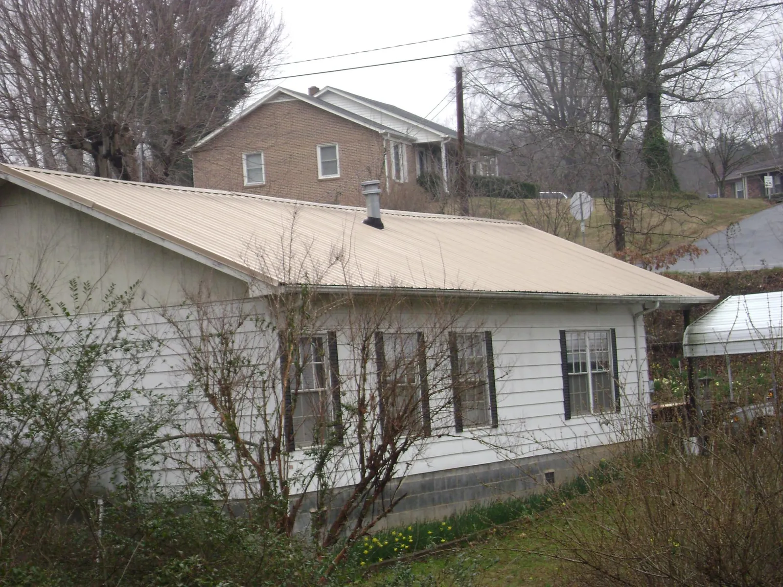 Tan metal roof on a white sided house set into a hillside — Commercial Roofing by Roofing Brothers in Harbeson