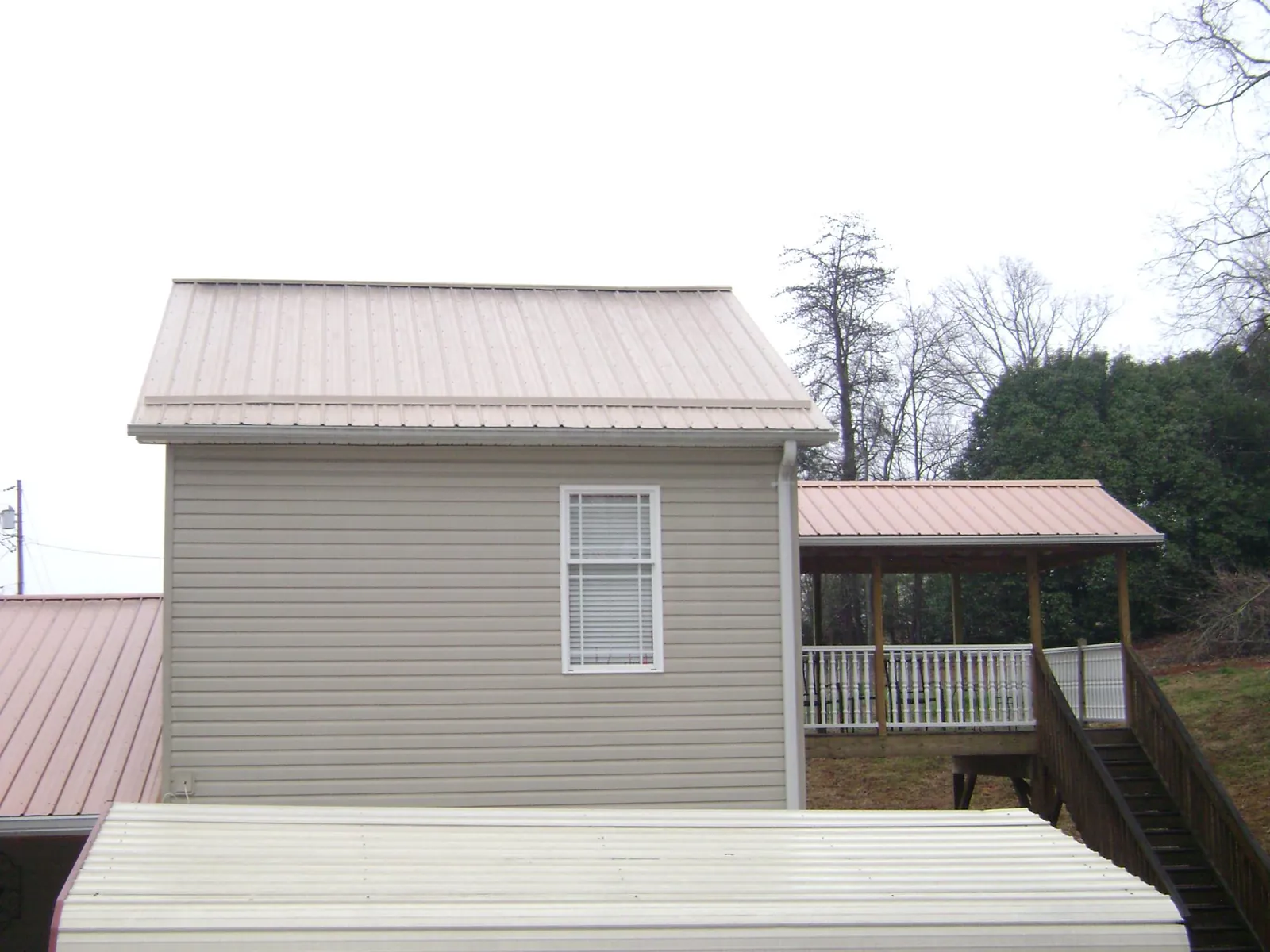 Tan metal roofs on a two story addition and attached porch, from a Roof Replacement job in Harbeson